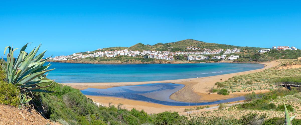 A coastal town with white buildings on a hillside, a sandy beach, and a clear blue sea.