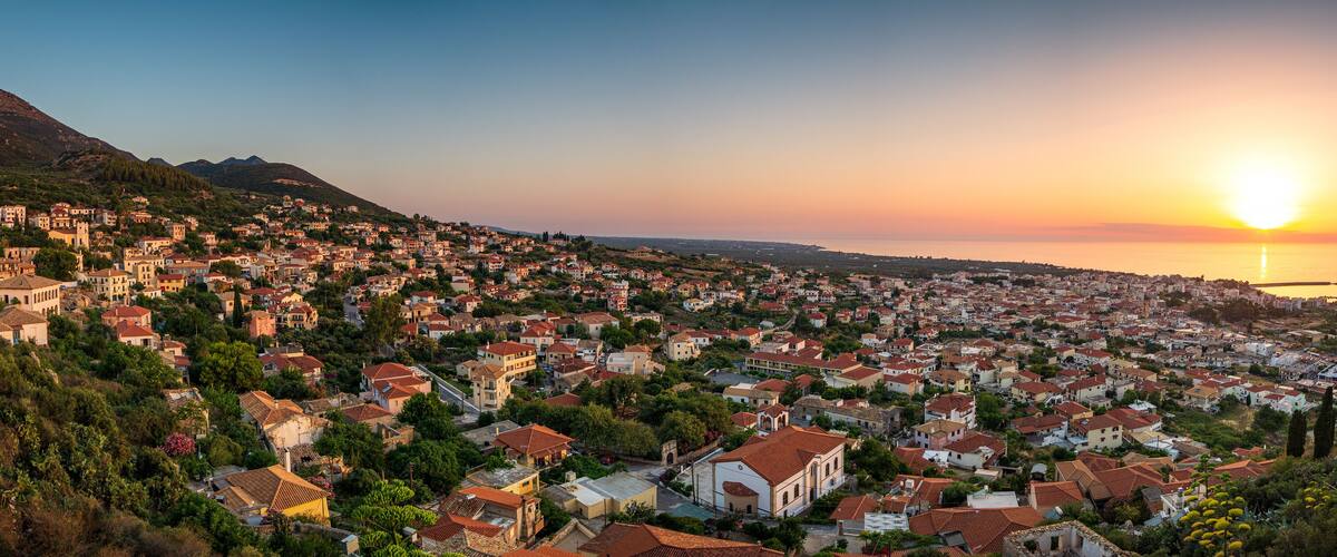 A coastal town at sunset with a mountain in the background.