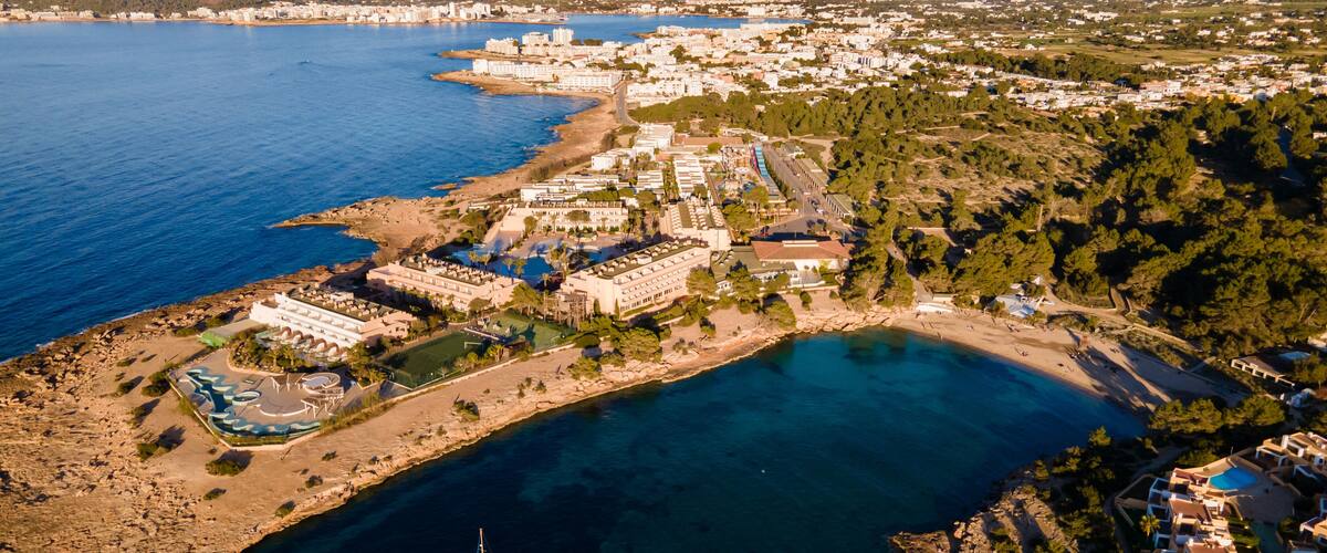 An aerial view of a coastal town with a marina, sandy beaches, and a mix of residential and commercial buildings.