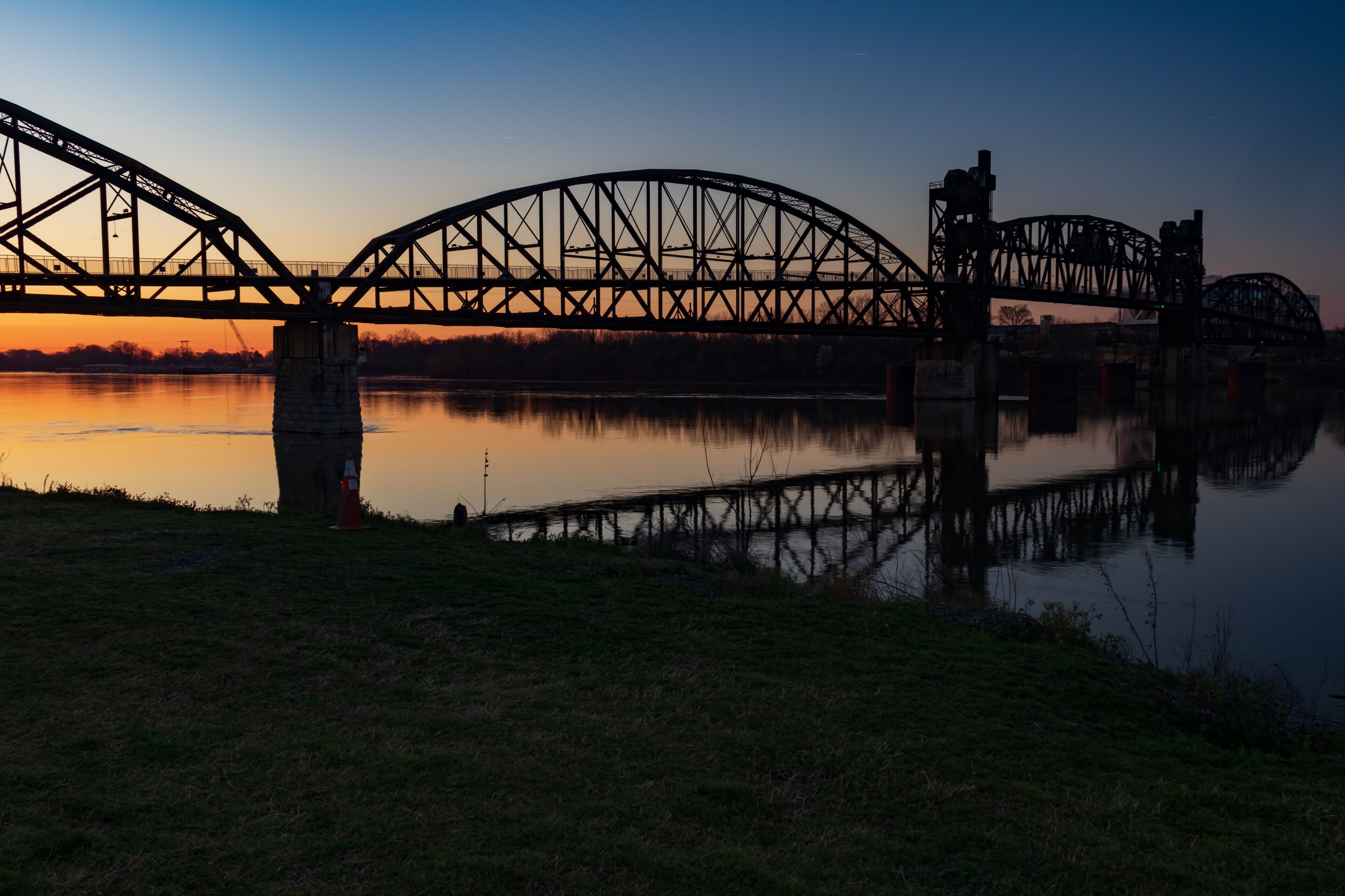 A steel bridge over a calm river at sunset.