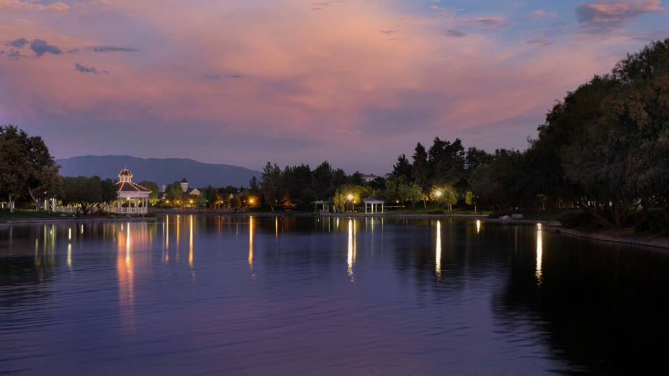A calm lake at dusk with a gazebo and trees reflecting on the water.