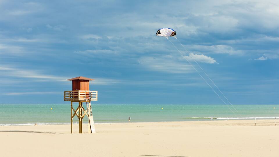 A beach with a lifeguard tower and a kite flying in the sky.
