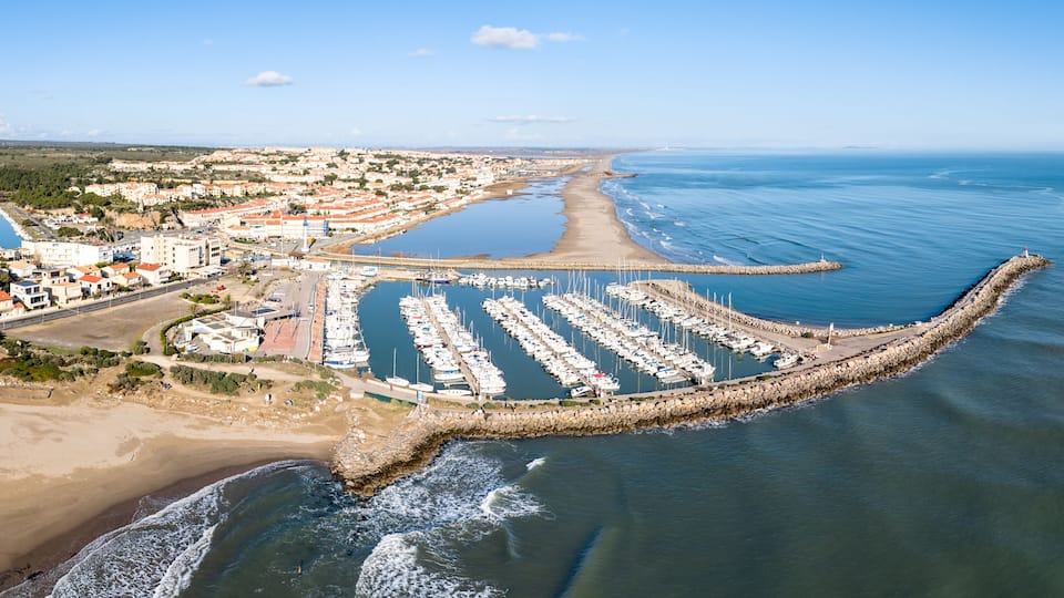 A coastal marina with boats, a beach, and a town in the background.