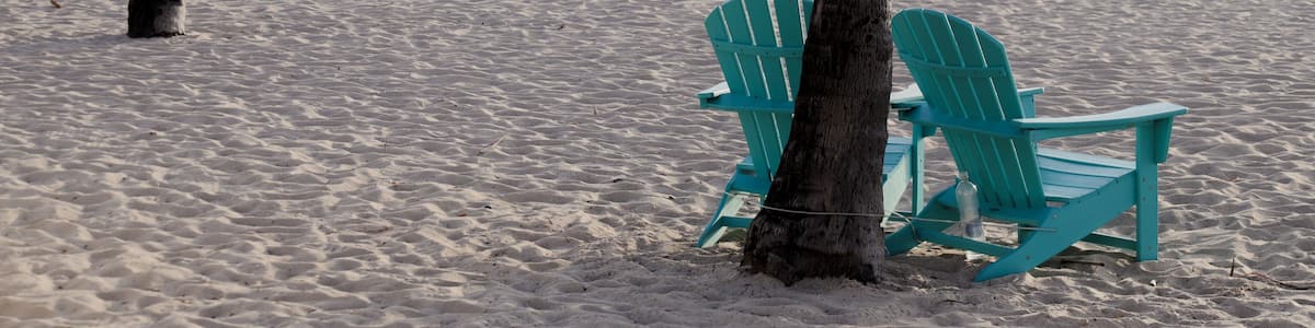 Une plage avec deux chaises Adirondack turquoise et un palmier.