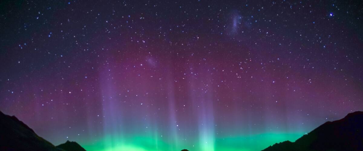 A night sky with the aurora borealis over a mountain range reflected in a lake.