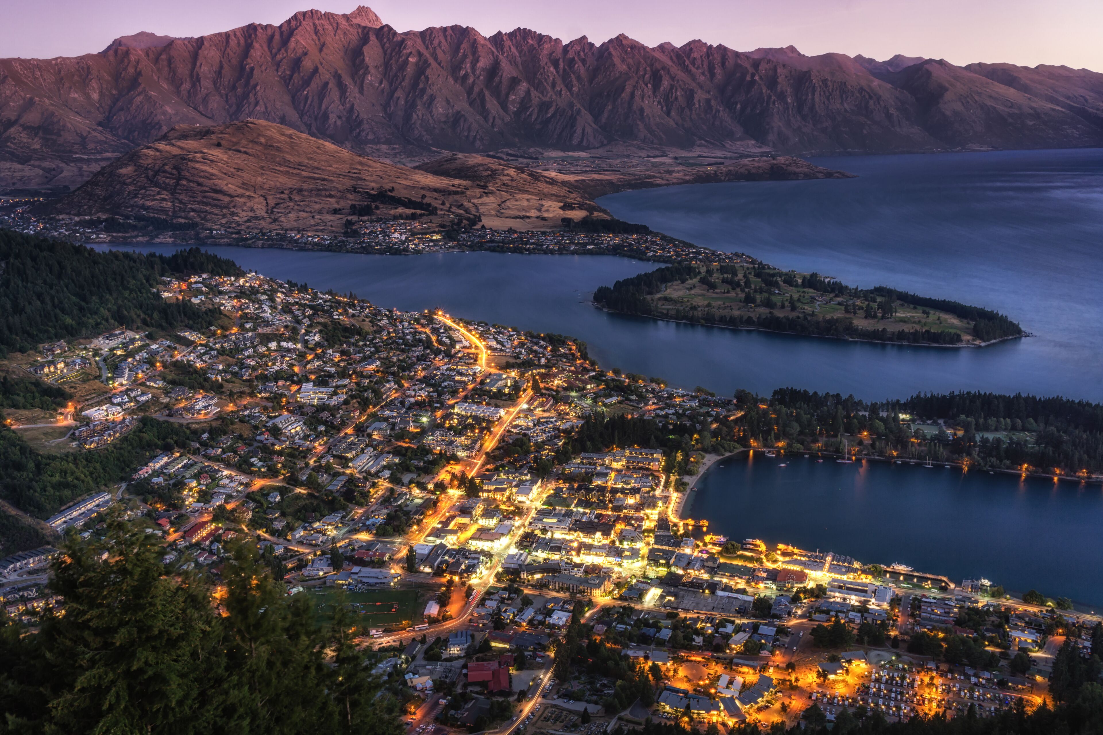 sunset view over queenstown in new zealand taken when the city is still lit up with lake wakatipu in the distance.