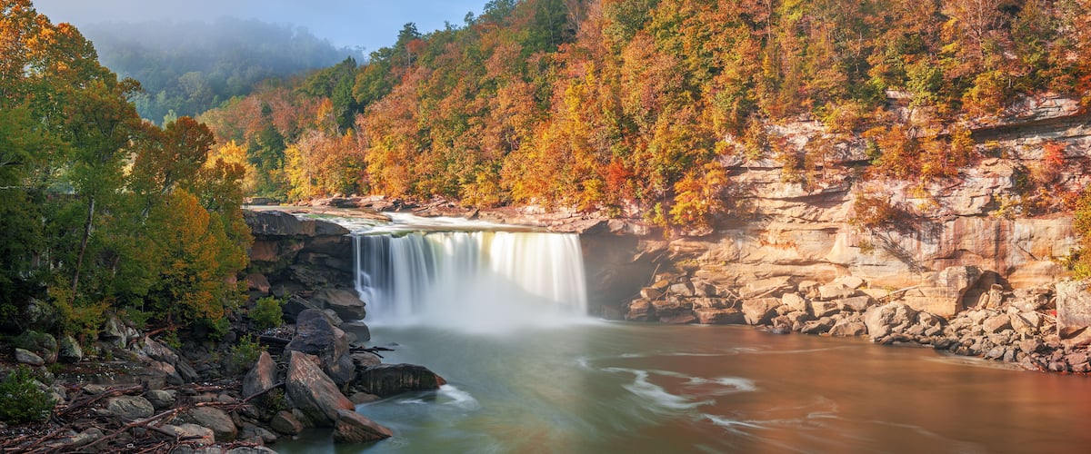 A waterfall cascading over a rocky cliff surrounded by autumn-colored trees.