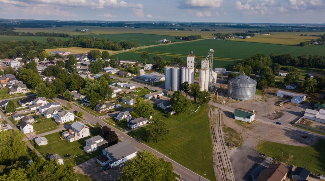 Aerial view of a rural town where silver grain silos pierce the skyline amidst a verdant landscape of fields and homes, West Liberty, Ohio, United States.