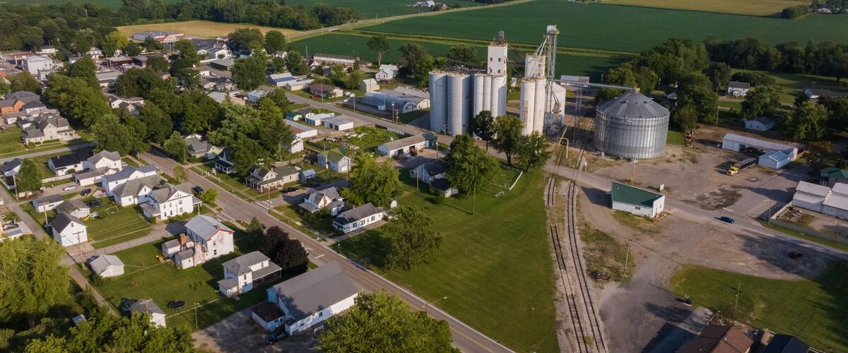 An aerial view of a rural town with residential houses, a grain silo, and a railway track.