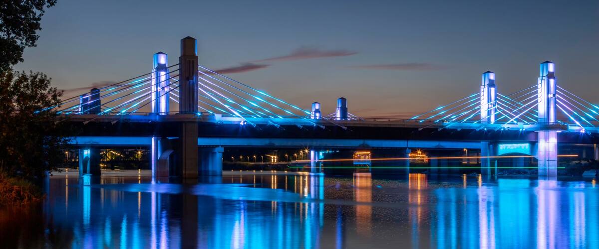 A bridge with illuminated blue lights reflecting on the water at dusk.