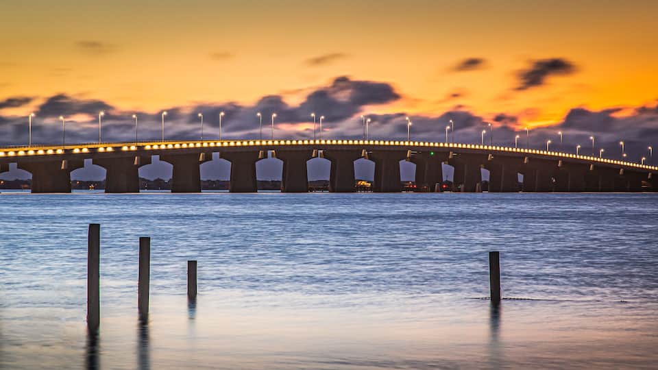 A bridge with streetlights at dusk over a calm body of water.