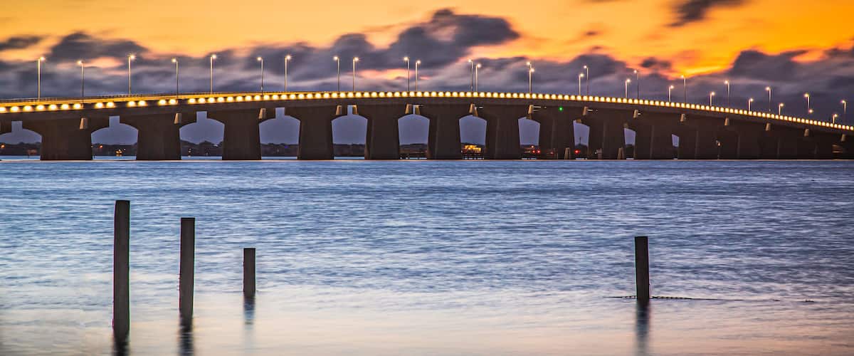 A bridge with streetlights at dusk over a calm body of water.