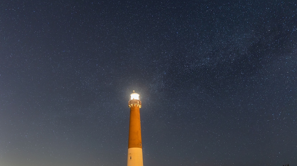 Path leading to a tall stone lighthouse with stars and the Milky Way in the night sky overhead. Barnegat Lighthouse State Park, New Jersey