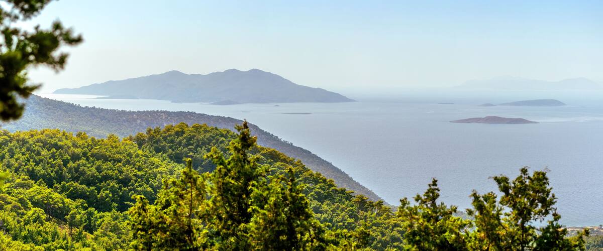A wide, hazy view from the western coast of Rhodes overlooks the Aegean Sea and islands Halki, Theodoros, Tragousa, Alimia, Marki, and Tilos in the distance.