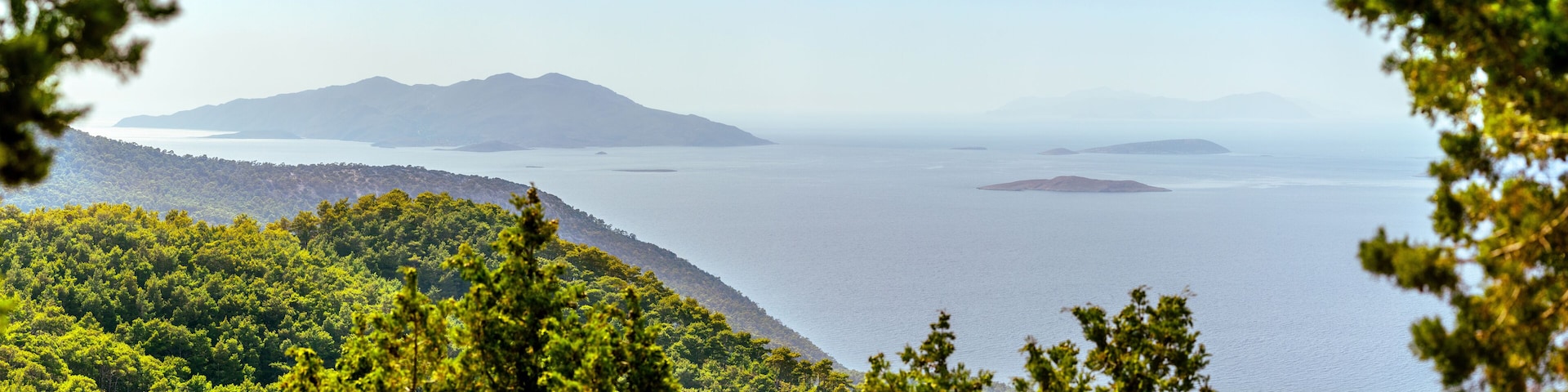A wide, hazy view from the western coast of Rhodes overlooks the Aegean Sea and islands Halki, Theodoros, Tragousa, Alimia, Marki, and Tilos in the distance.
