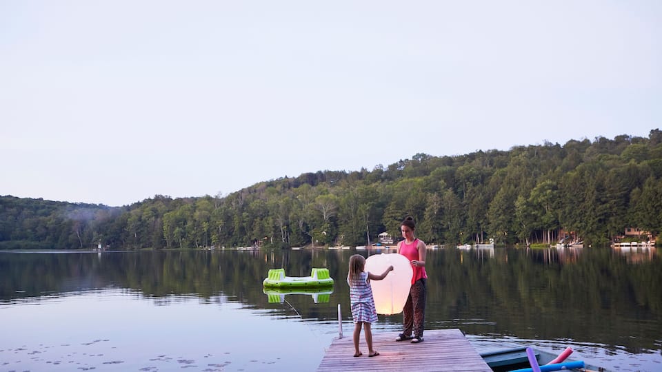 A calm lake with a wooden dock, a green inflatable raft, and a woman and child holding a large white object.