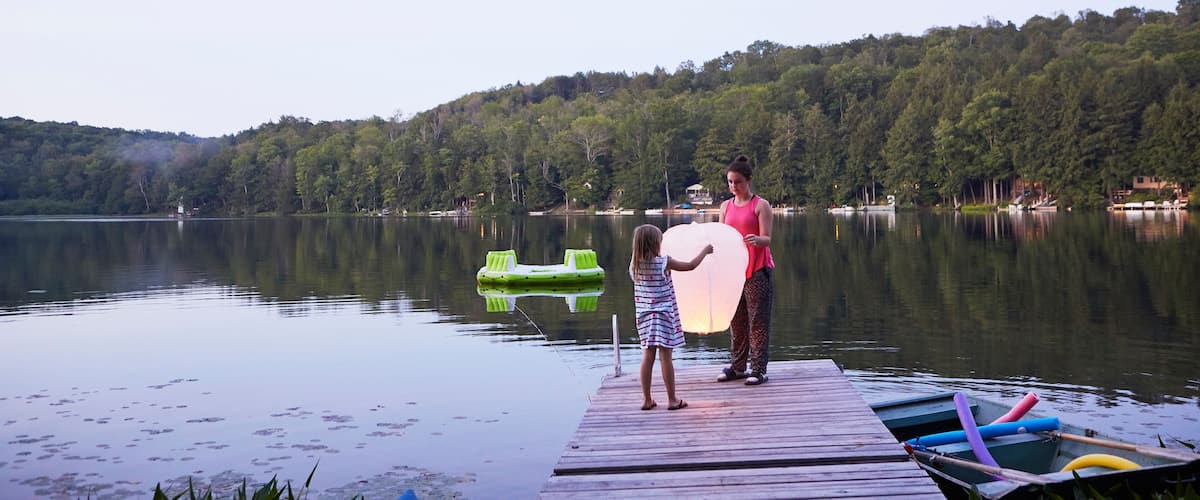 A calm lake with a wooden dock, a green inflatable raft, and a woman and child holding a large white object.