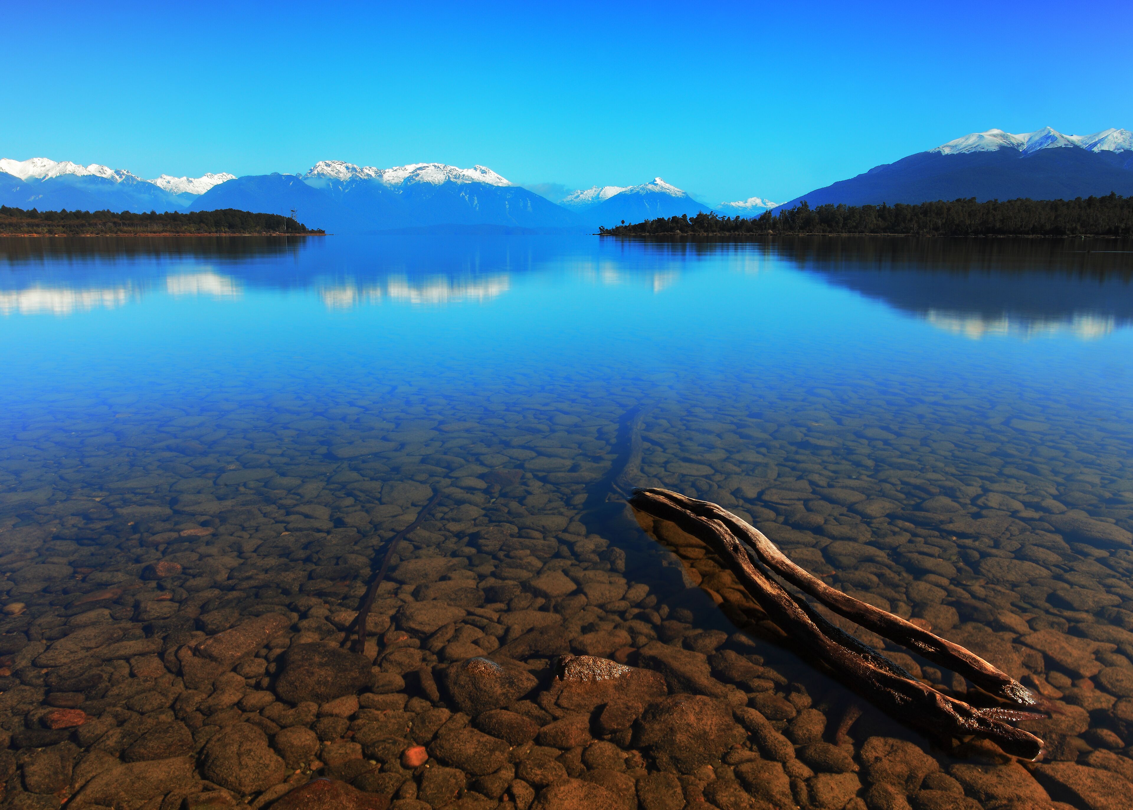 A clear lake with a rocky shore and mountains in the background.