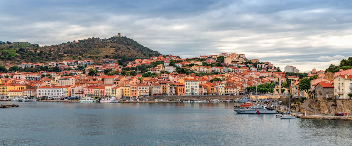 A coastal town with colorful buildings, a hilltop fortress, and a marina with boats.