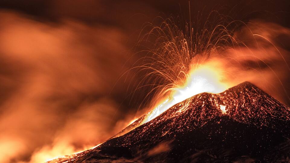 A volcano erupting with glowing lava and bright sparks.