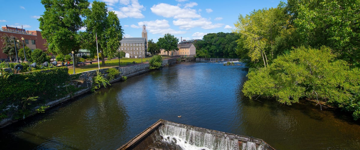 A river with a waterfall, surrounded by trees and buildings.