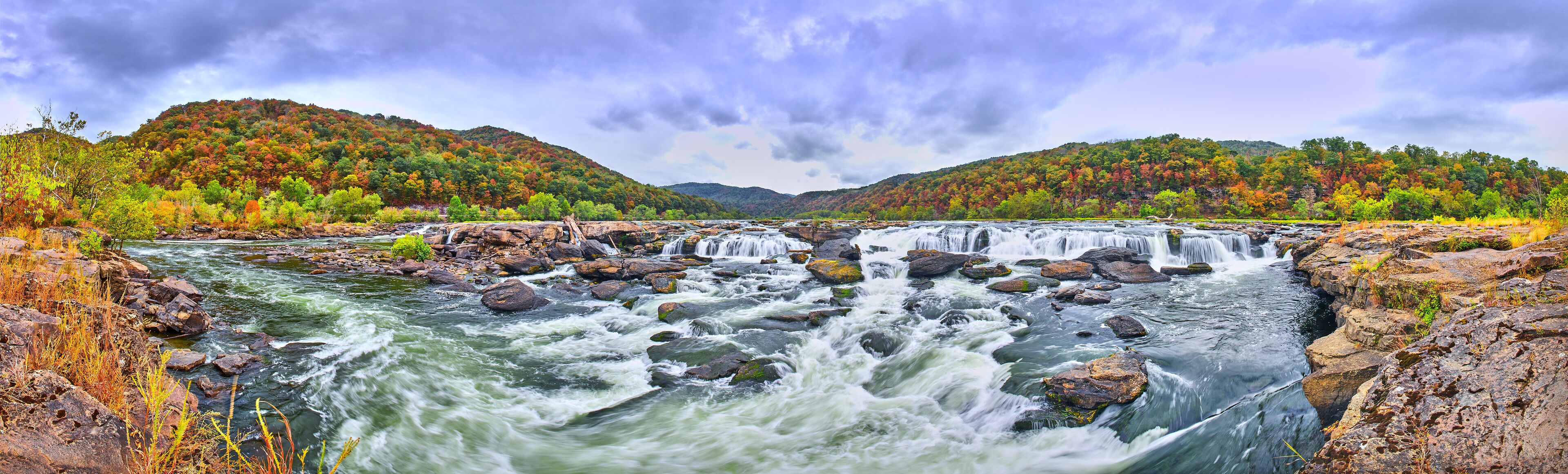A river with multiple waterfalls surrounded by autumn-colored trees and hills.