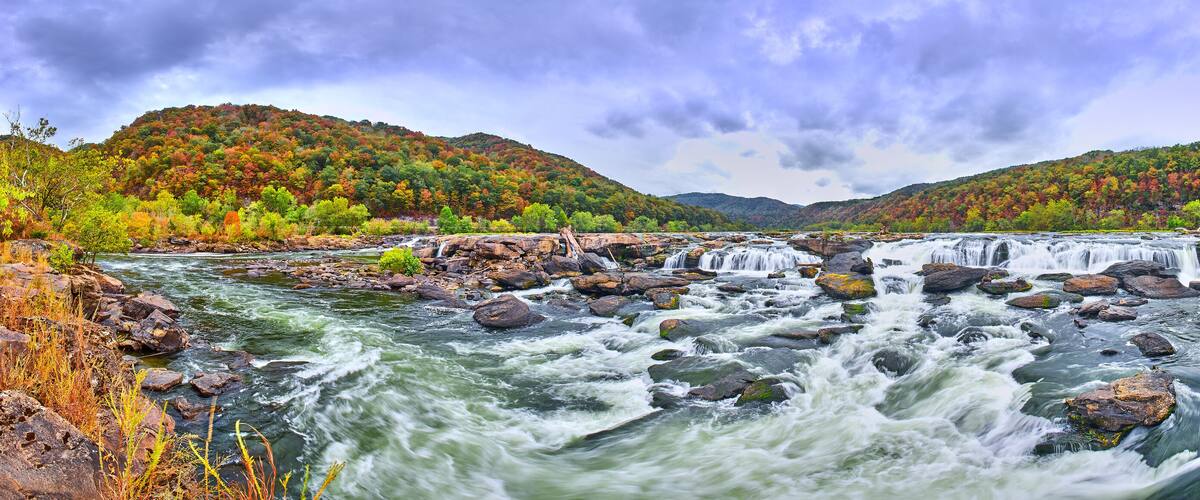 A river with multiple waterfalls surrounded by autumn-colored trees and hills.
