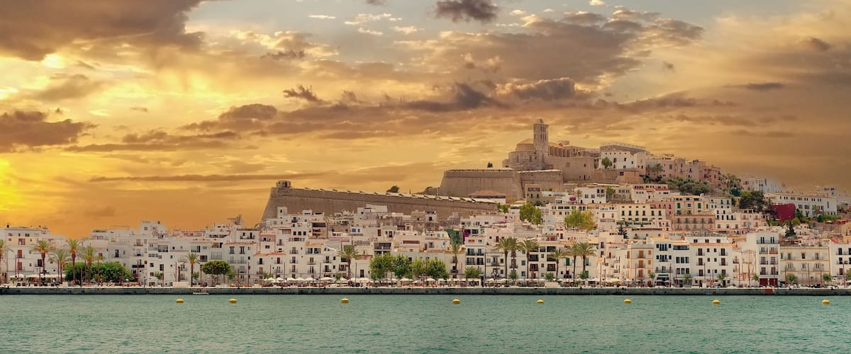A coastal cityscape with a prominent hilltop fortress and white buildings along the waterfront.