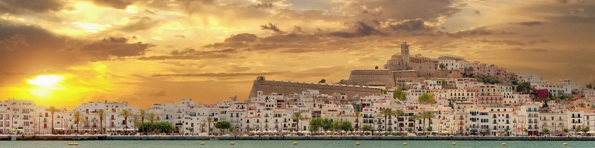 A coastal cityscape with a prominent hilltop fortress and white buildings along the waterfront.