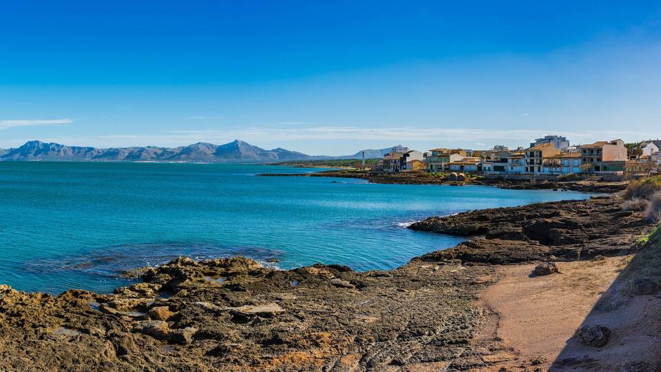 A coastal town with a rocky shoreline, a wooden boardwalk, and buildings along the sea.