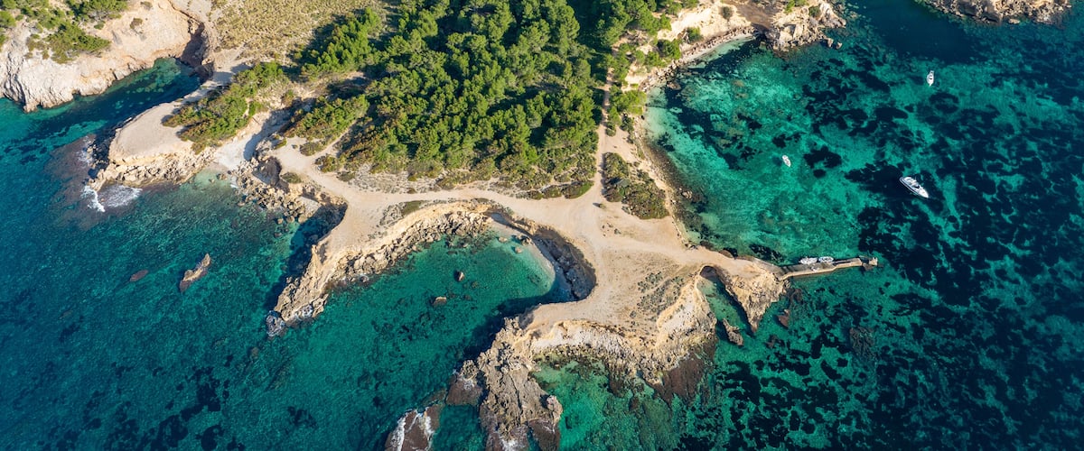 Vista aérea de uma área costeira com águas turquesas cristalinas, costas rochosas e florestas verdejantes densas.