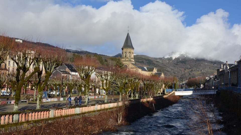 A river flowing through a town with a church and mountains in the background.