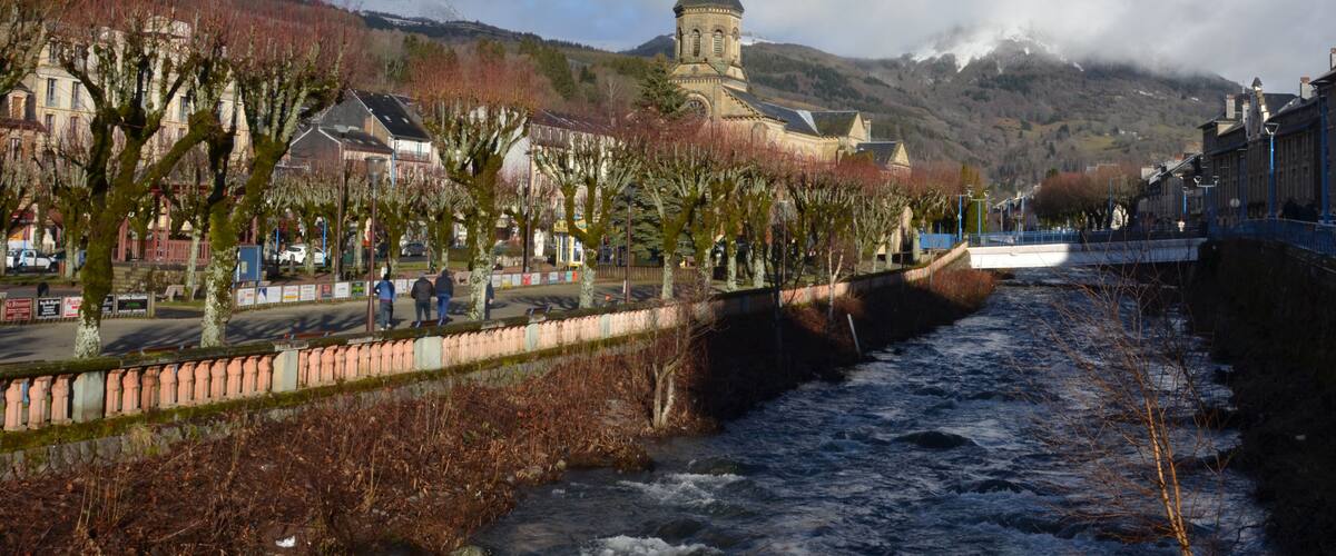 A river flowing through a town with a church and mountains in the background.