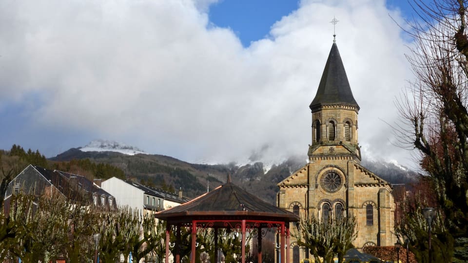 A church with a tall spire, a gazebo, and a mountain in the background.