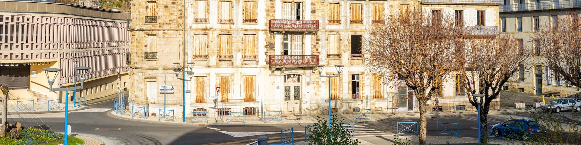 A historic stone building with multiple balconies and a turret, surrounded by a modern urban environment with a clear sky.