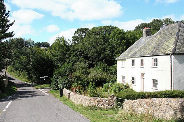 Une route de campagne bordée d’une maison blanche, d’un mur de pierres et d’une végétation luxuriante.