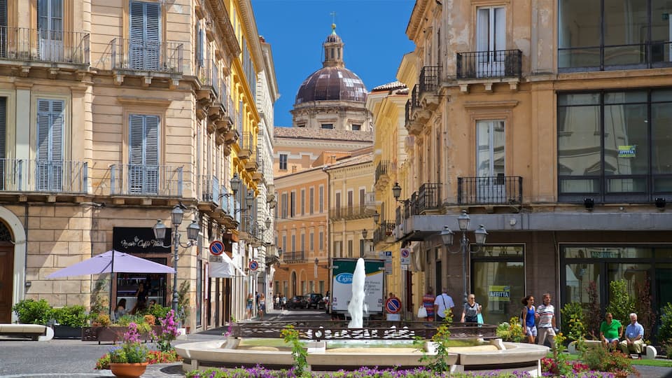 A historic square with a fountain, ornate buildings, and a domed structure in the background.
