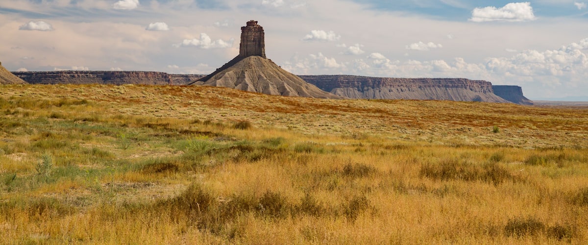 A flat terrain with a prominent rock formation in the center and a distant cliff.