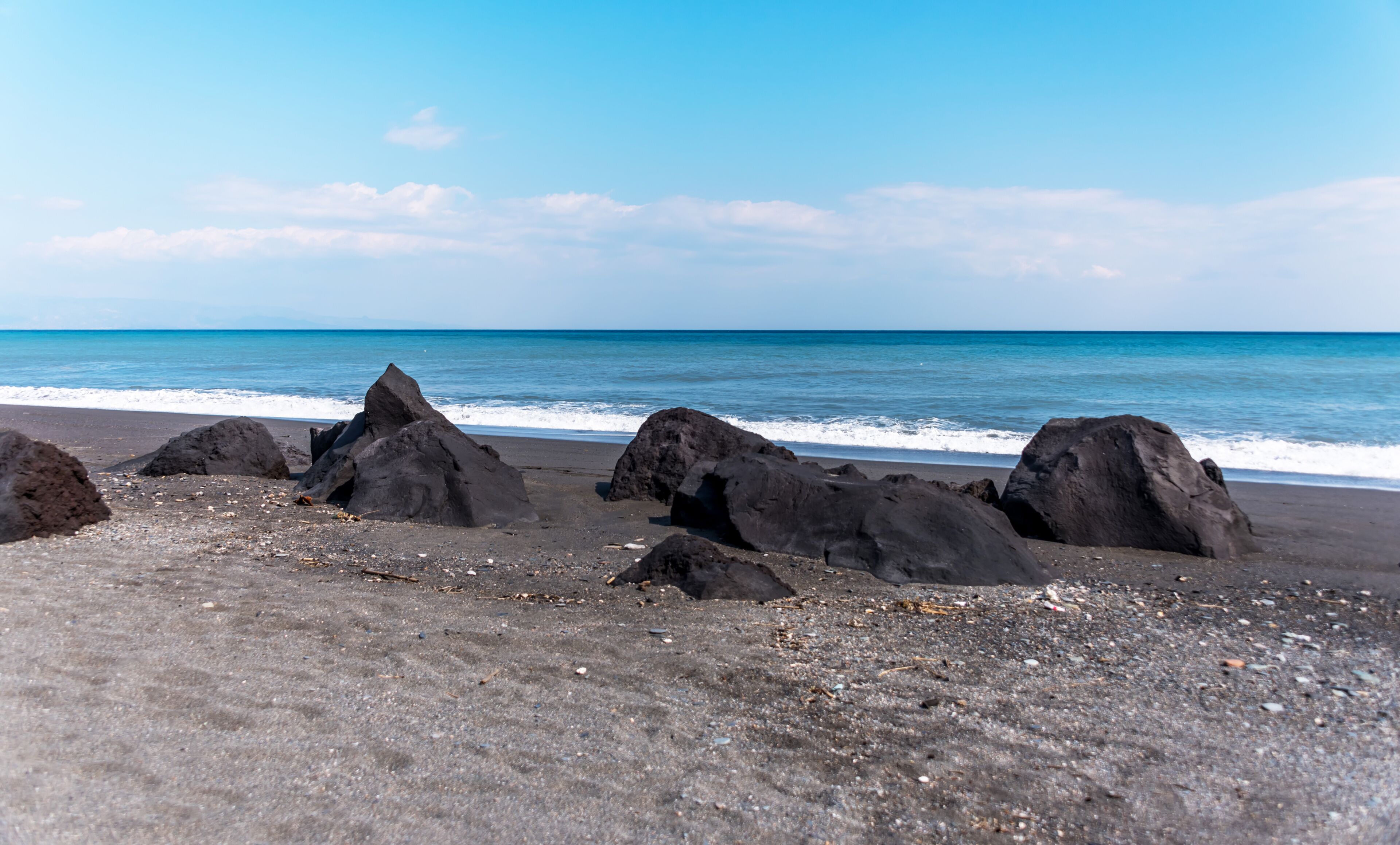 A beach with large dark rocks and a calm sea.