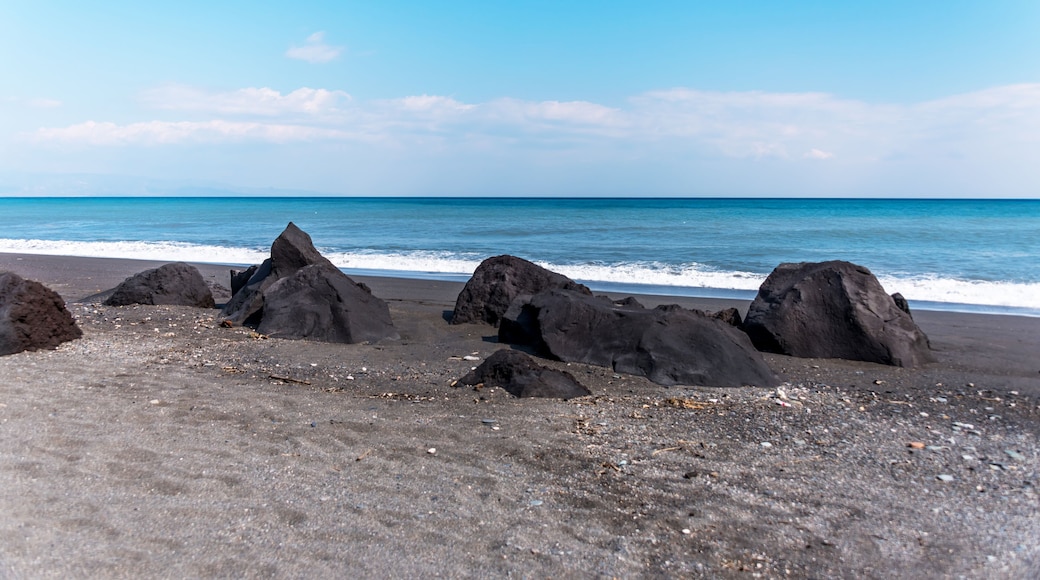 A beach with large dark rocks and a calm sea.