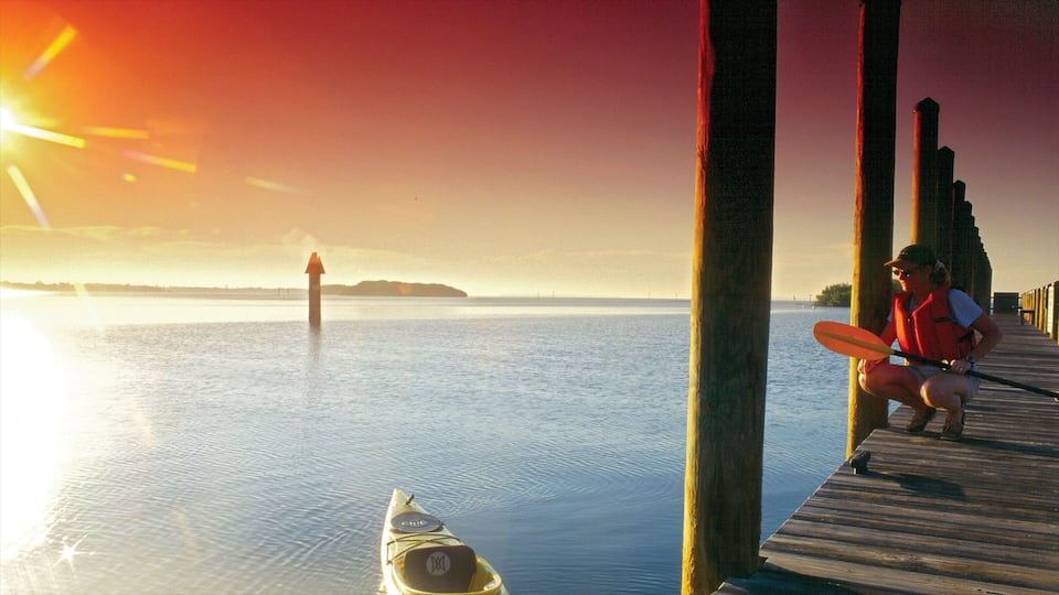 A wooden pier extending into calm water with a kayak and a person in a life jacket.