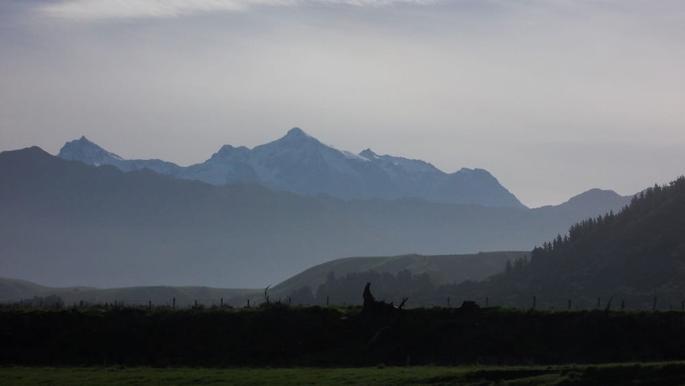 A mountain range with a person standing on a hill.
