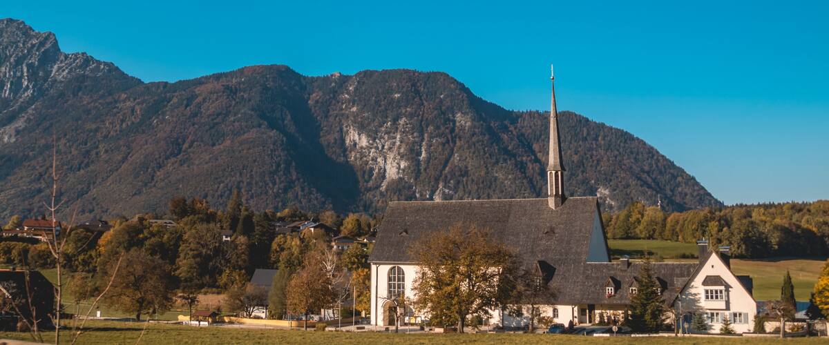 A church with a tall steeple, surrounded by houses and a mountain range in the background.