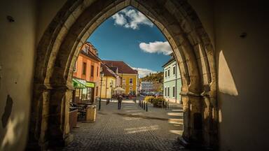 A cobblestone street through an arched stone gateway with colorful buildings.
