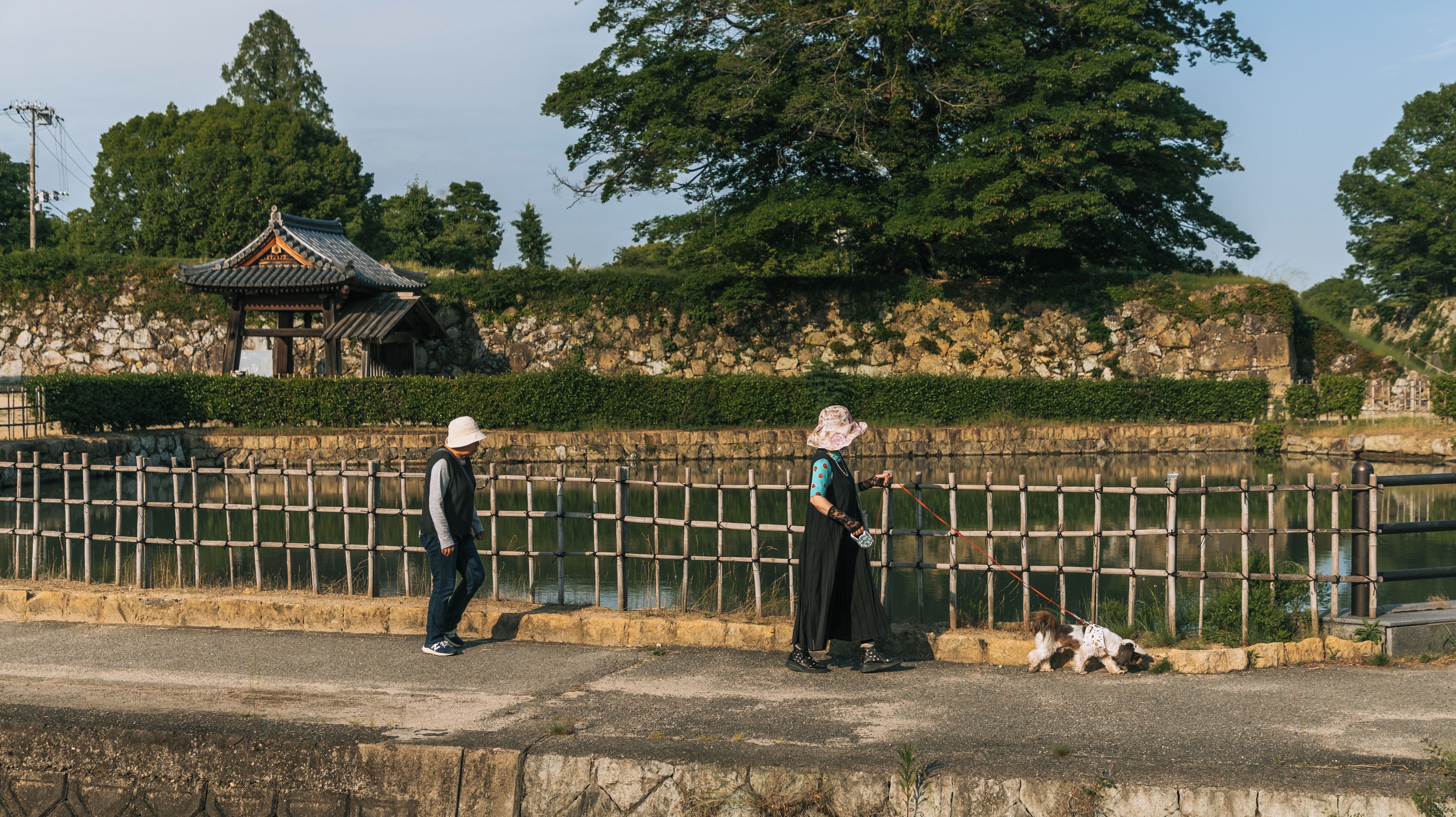 A traditional pavilion, a stone wall, and a wooden fence by a body of water.