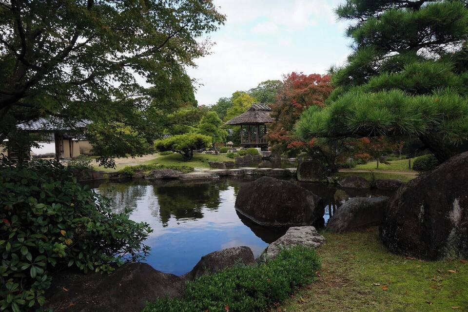A tranquil garden with a pond, rocks, and a traditional gazebo.