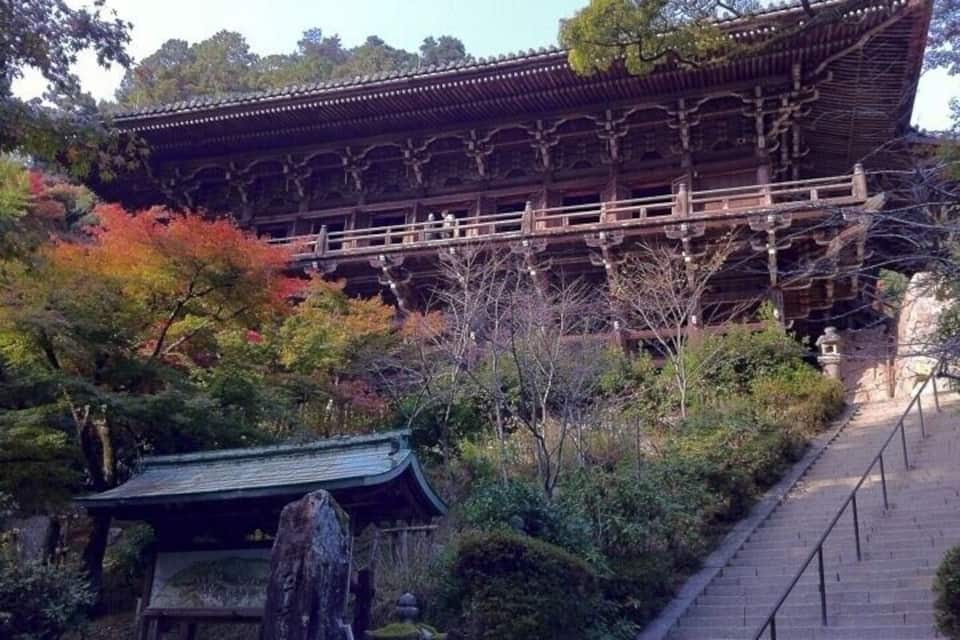 A traditional Japanese building with a wooden structure and a stone base, surrounded by autumn-colored trees and a stone pathway.