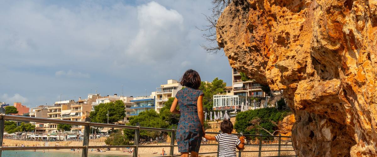 A rocky coastline with a woman and child walking along a paved path.