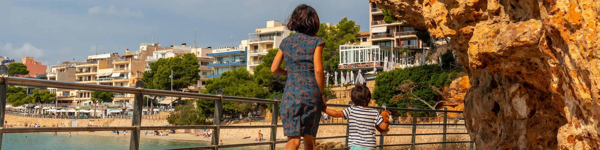 A rocky coastline with a woman and child walking along a paved path.