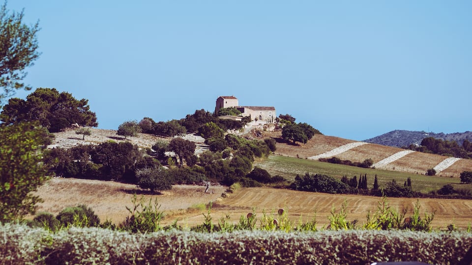 A rural landscape with a stone building on a hill, surrounded by trees and fields.